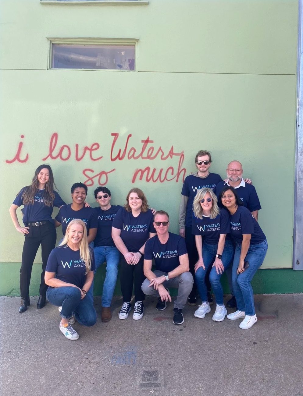 The Waters team in branded T-shirts in front of an “i love Waters so much” mural